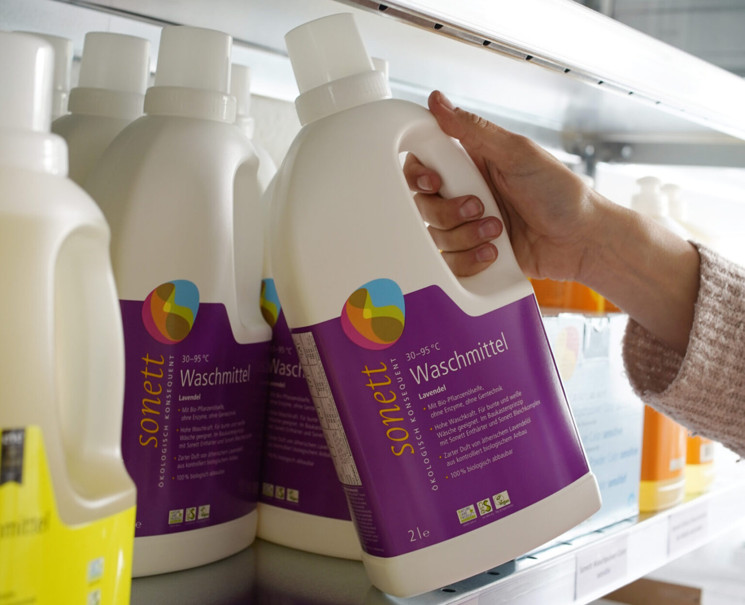 Eine Person nimmt eine Flasche Waschmittel aus einem Regal